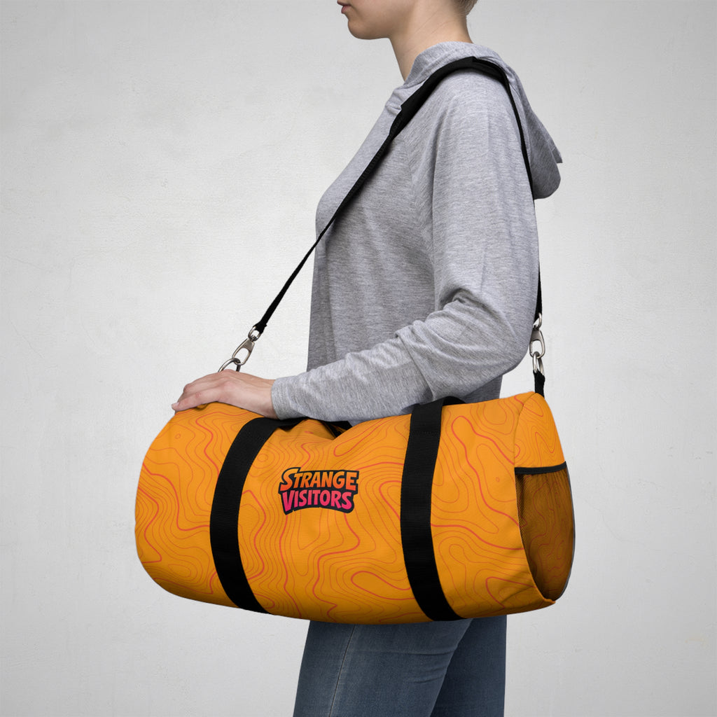 Pack For The Unknown duffel: an orange barrel-style duffel bag covered in topographic contour lines with the Strange Visitors logo, black zipper and black carry handles (view 5)