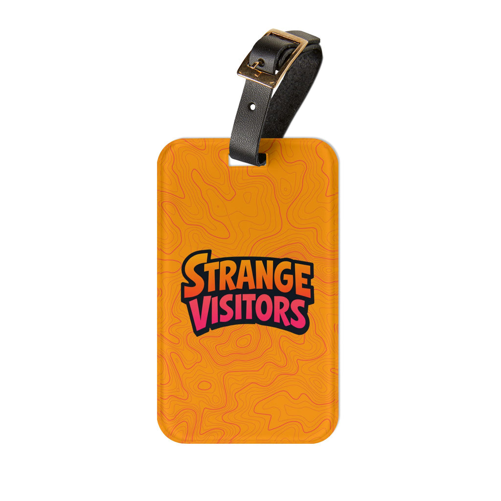 Extra Baggage luggage tag: a glossy orange acrylic tag covered in topographic contour lines with the Strange Visitors logo, on a black leather strap with a buckle